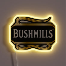 Charger l&#39;image dans la galerie, Neon sign shaped like the Bushmills whiskey logo with white text on a black and gold background, glowing with a warm yellow outline.

