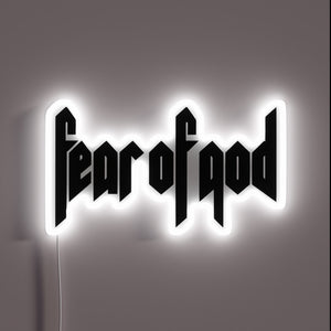 Alt text: "Neon sign displaying the phrase 'fear of god' in bold, gothic-style black lettering, outlined with a glowing white border."
