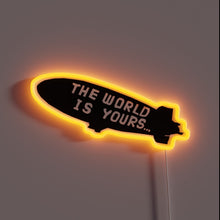 Charger l&#39;image dans la galerie, This neon sign evokes the iconic blimp message from *Scarface*: **“The World Is Yours…”** — a bold, cinematic reminder to dream big and chase everything. 🛩️🔥